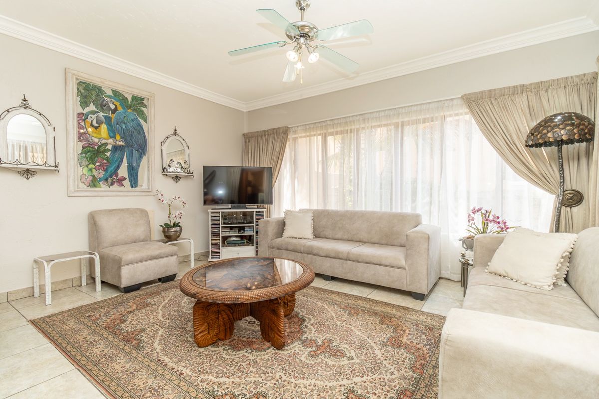 A bright and spacious living room featuring tiled flooring, crown molding, and a ceiling fan, with large windows providing ample natural light.