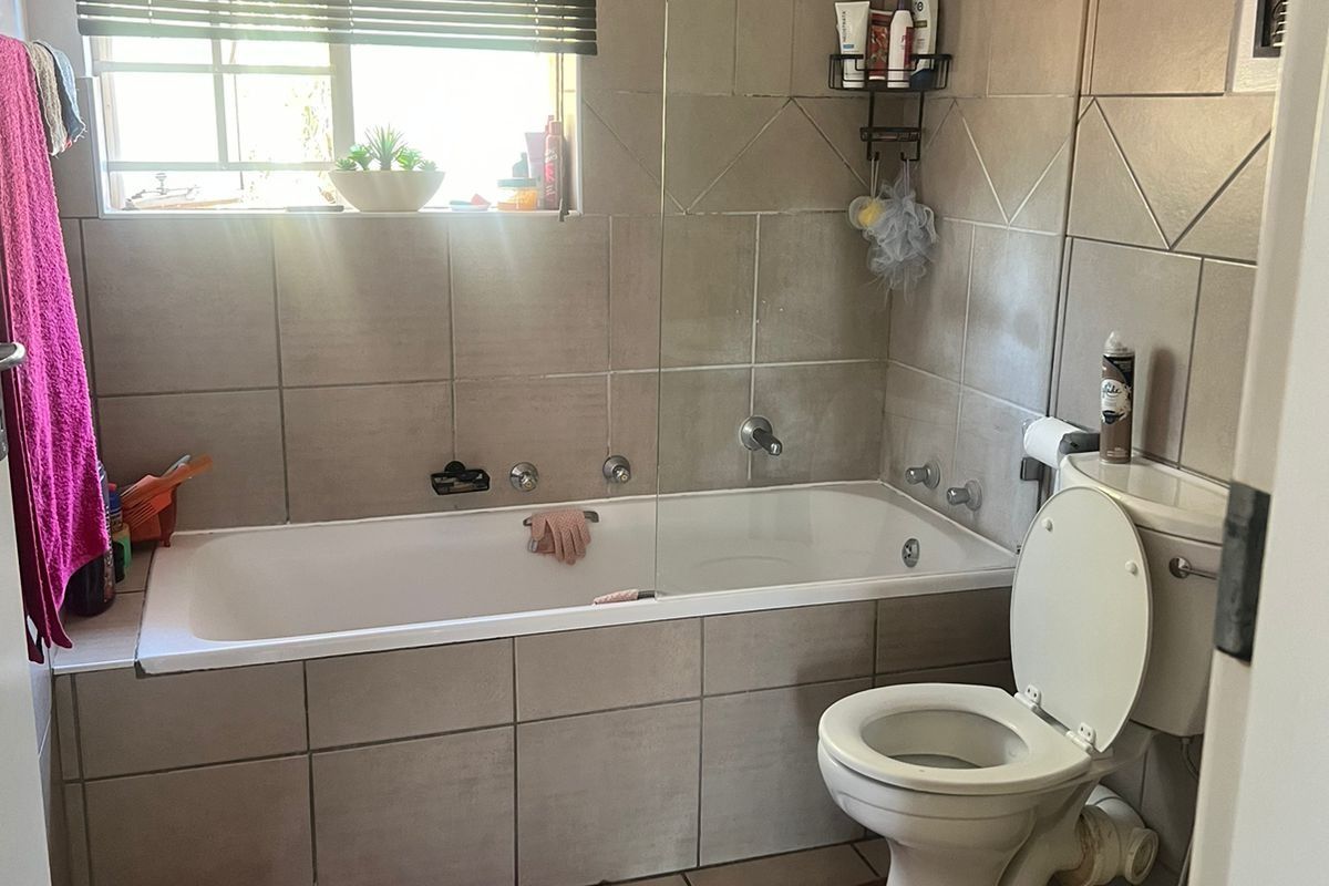 A functional bathroom featuring a tiled bathtub with an integrated shower, glass screen, and standard toilet suite.
