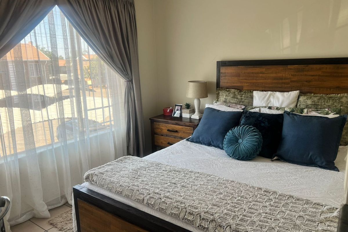 A well-lit bedroom featuring tiled flooring and a large window with curtain treatments, providing a comfortable and functional living space.
