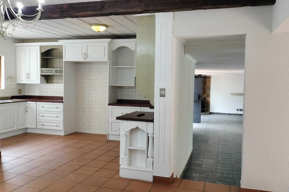 A kitchen featuring white cabinetry, tiled countertops, and terracotta flooring, with an adjacent room visible through a doorway.