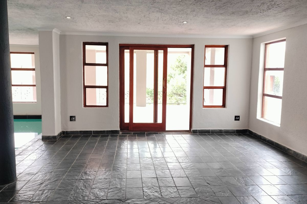 Spacious living area featuring dark slate tile flooring, large wooden-framed sliding doors leading to the outdoors, and a view of the adjacent swimming pool.