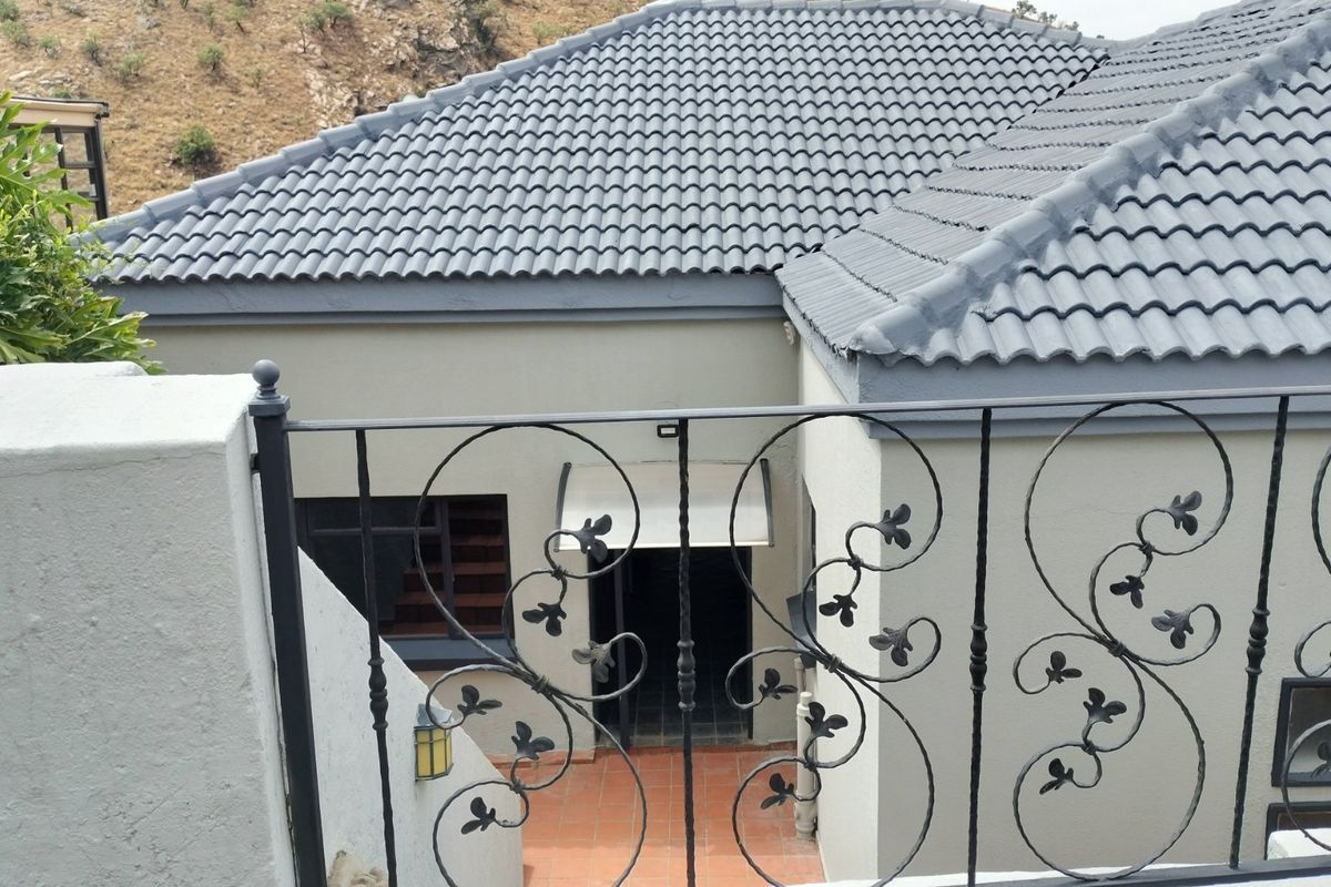 View of the rear exterior elevation featuring a tiled roof, wrought iron balustrade, and a paved patio area.