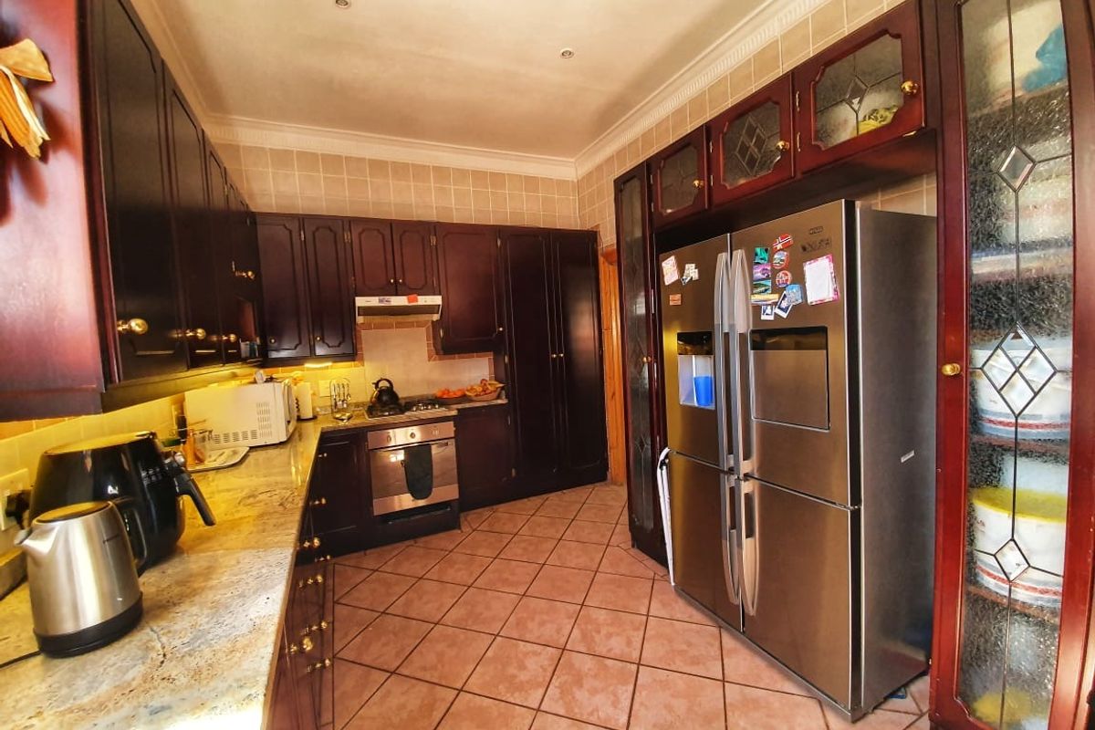 A traditional kitchen featuring dark wood cabinetry, granite countertops, tiled flooring, and built-in stainless steel oven and extractor fan.