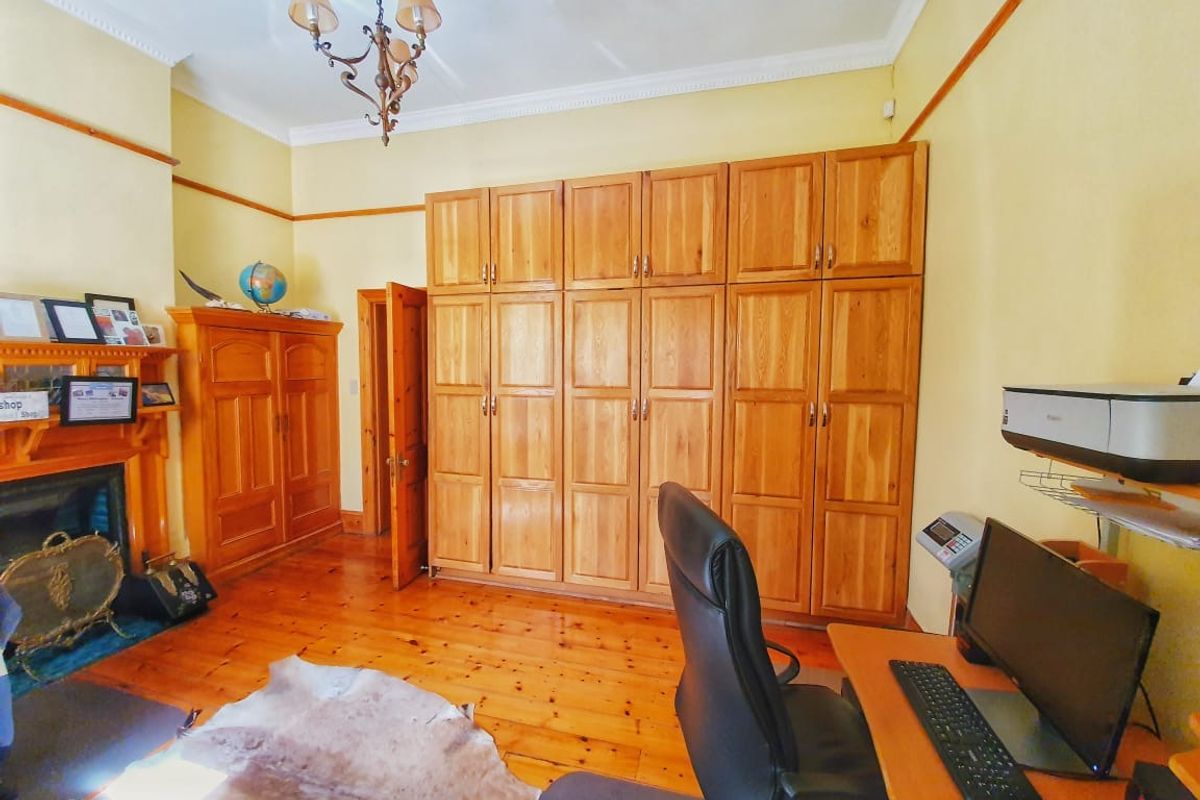 A spacious bedroom featuring extensive built-in timber cabinetry, polished wooden flooring, and a traditional fireplace surround, offering ample storage and classic character.