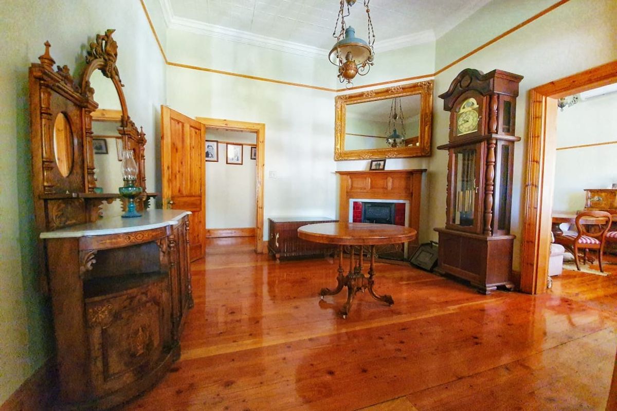 A spacious living room featuring polished timber flooring, a traditional fireplace with a wooden mantel, and decorative ceiling detailing.