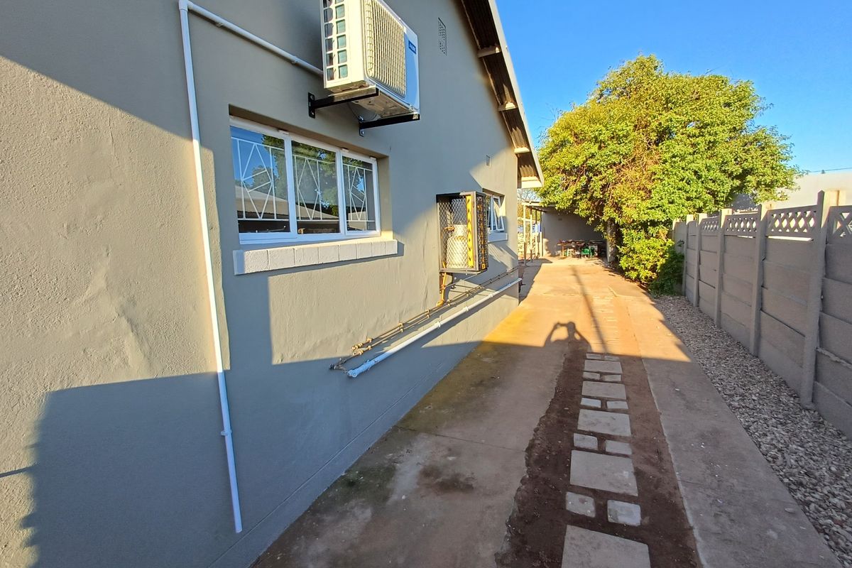 Side exterior view of the property featuring a concrete pathway, security window bars, and an externally mounted air conditioning unit.