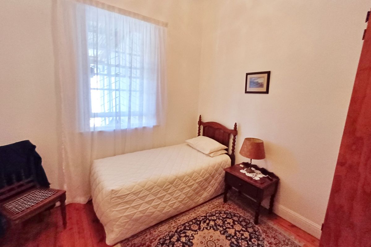 A cozy bedroom featuring polished timber flooring, a window with security bars, and neutral wall finishes.