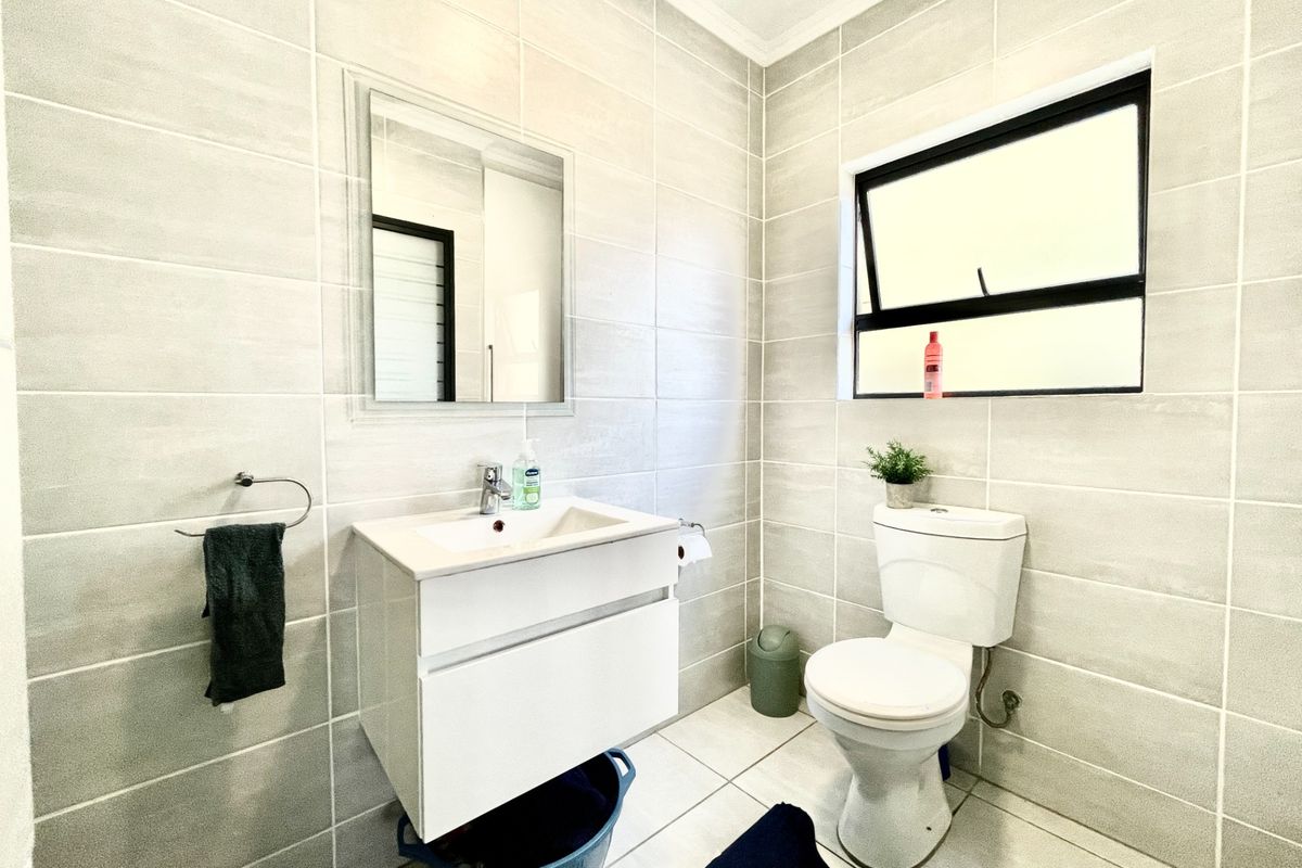 A modern bathroom featuring floor-to-ceiling light grey tiling, a wall-mounted vanity with a basin, and a standard toilet.