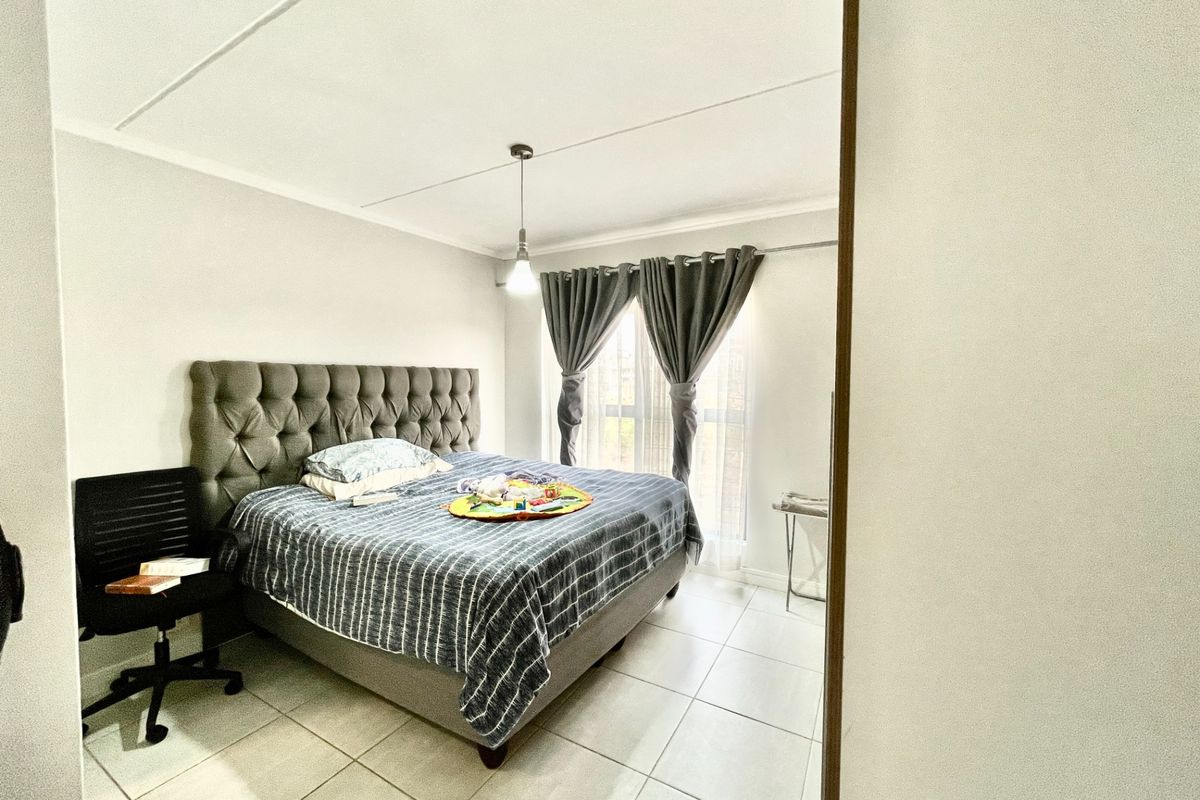 A bedroom featuring tiled flooring, a central pendant light, and a window with curtain tracks.