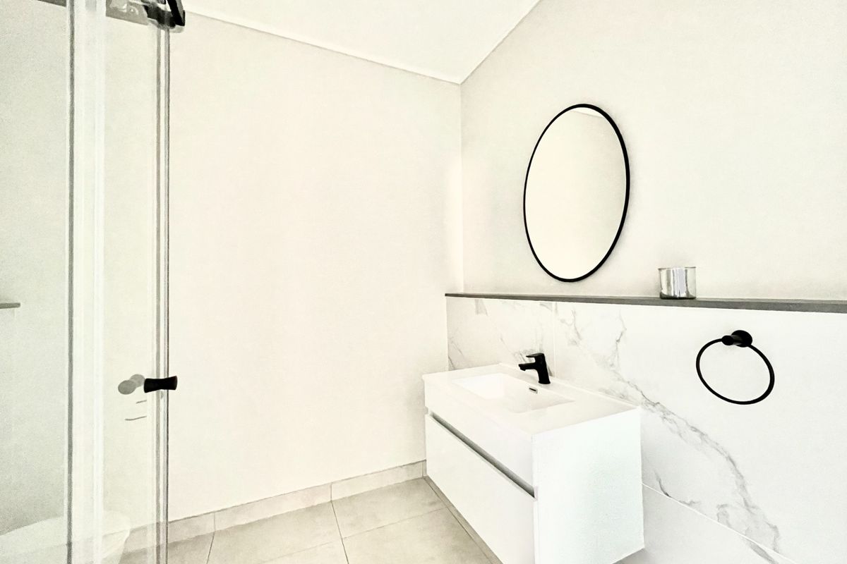 Modern bathroom featuring a floating vanity with marble-look splashback, black fixtures, and a glass-enclosed shower.