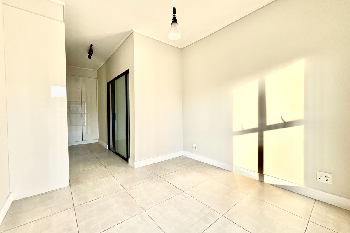 A bright, modern, and empty living area featuring neutral tiled flooring, clean white walls, and a sleek sliding glass door leading to an adjacent space.