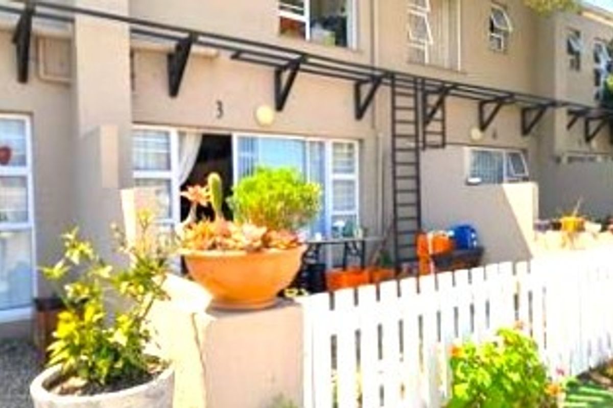 Exterior view of a townhouse featuring a private patio area, white picket fencing, and metal awning structures over the ground floor entrance.