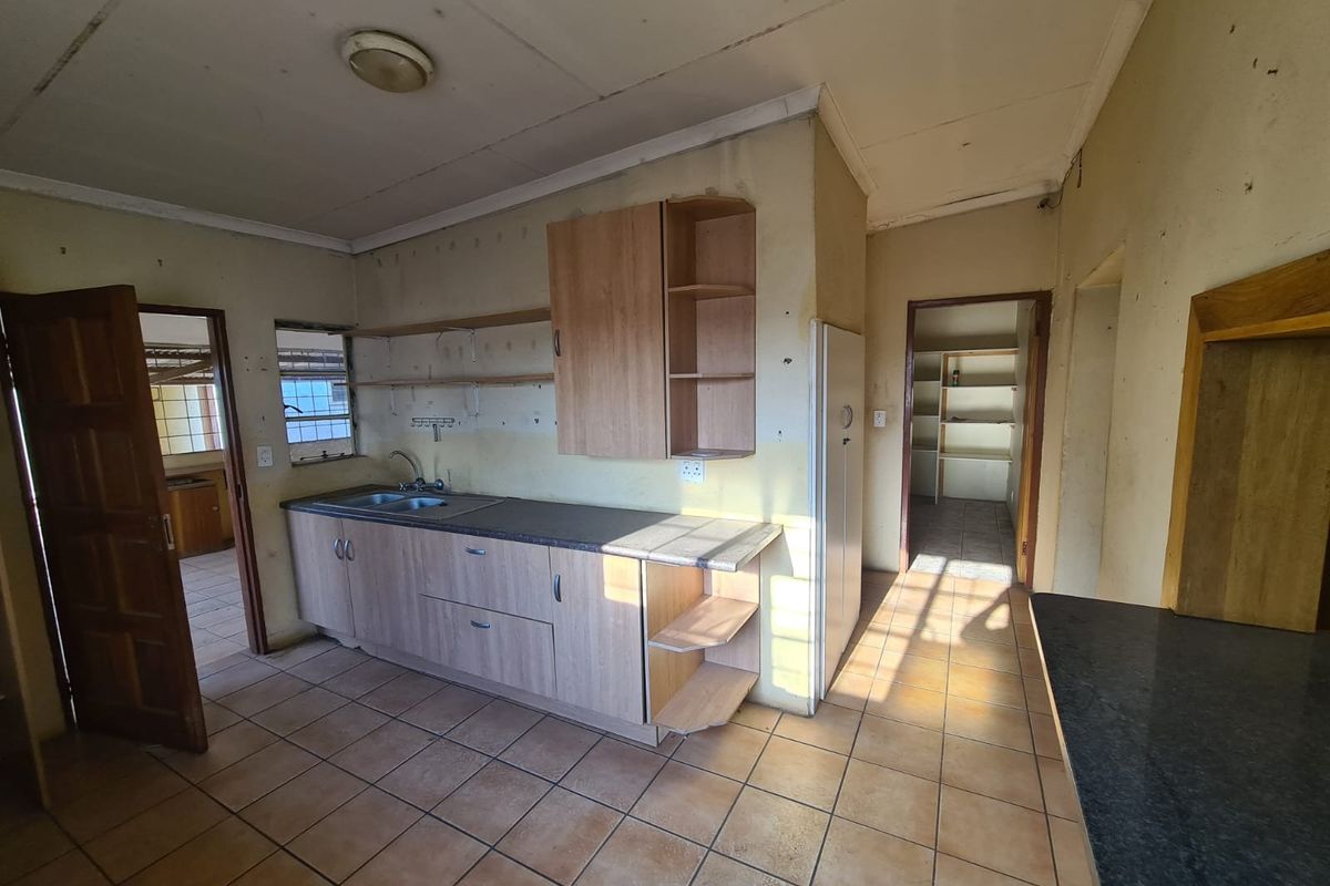 A dated kitchen featuring tiled flooring, built-in cabinetry, a double sink, and an adjacent pantry area, requiring cosmetic updates and maintenance.