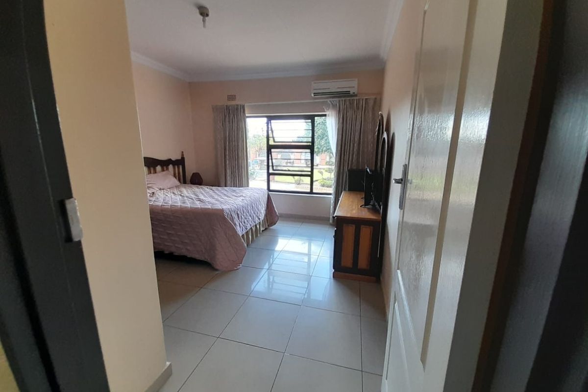 A well-lit bedroom featuring tiled flooring, a wall-mounted air conditioning unit, and a large window providing natural light.