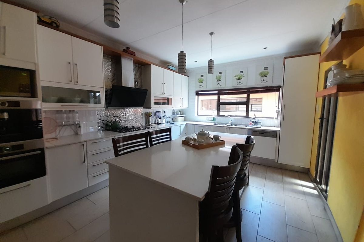 Modern kitchen featuring white cabinetry, stone countertops, a central island, built-in oven, and tiled flooring with ample natural light.