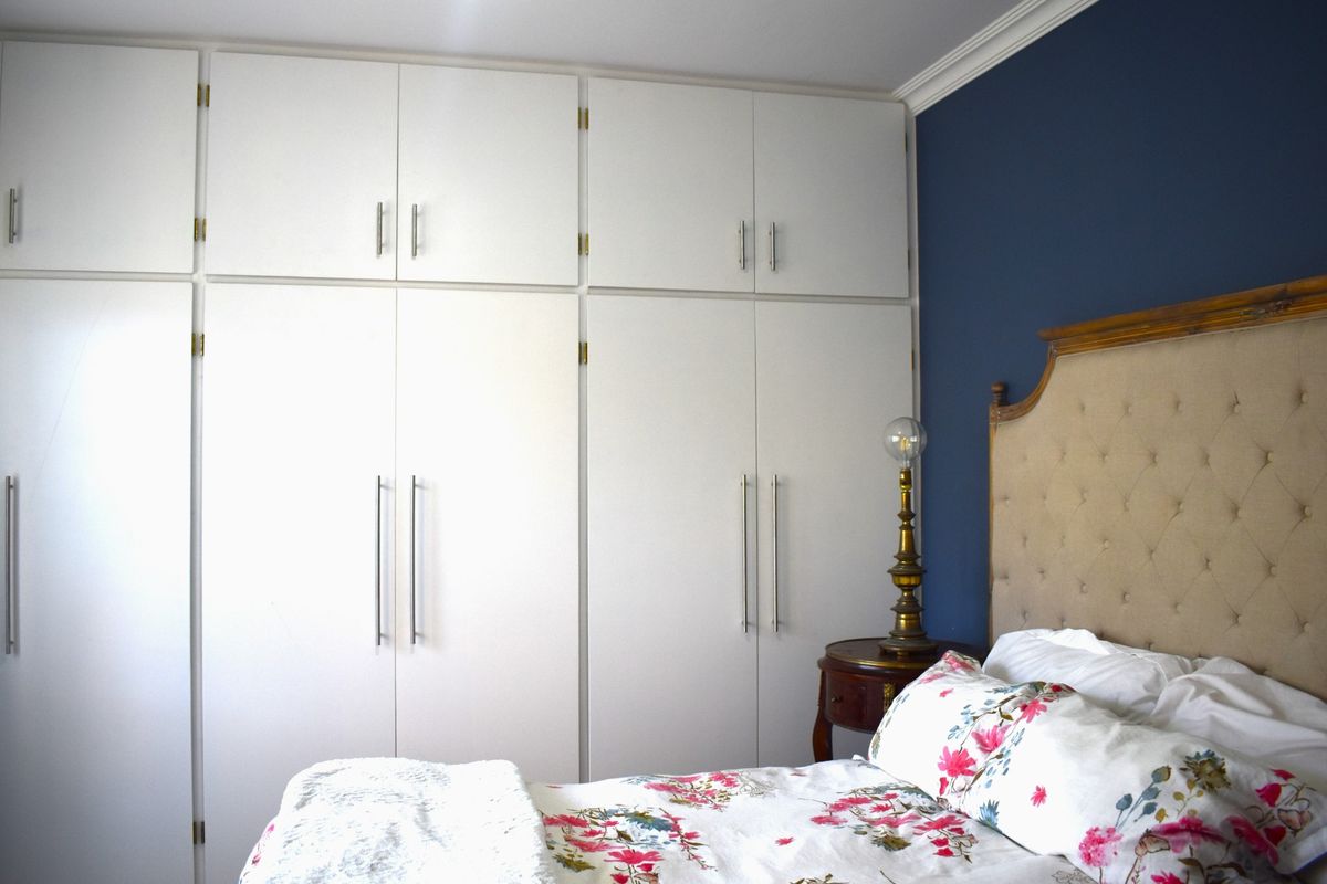 A well-maintained bedroom featuring extensive floor-to-ceiling built-in cabinetry with modern hardware and a contrasting feature wall.