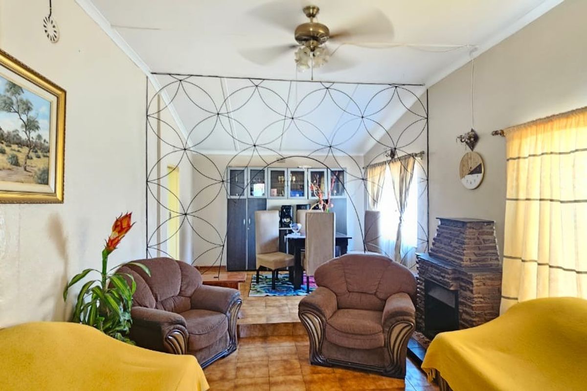 A living area featuring a stone-clad fireplace, ceiling fan, and a decorative metal room divider separating the space from the dining area.