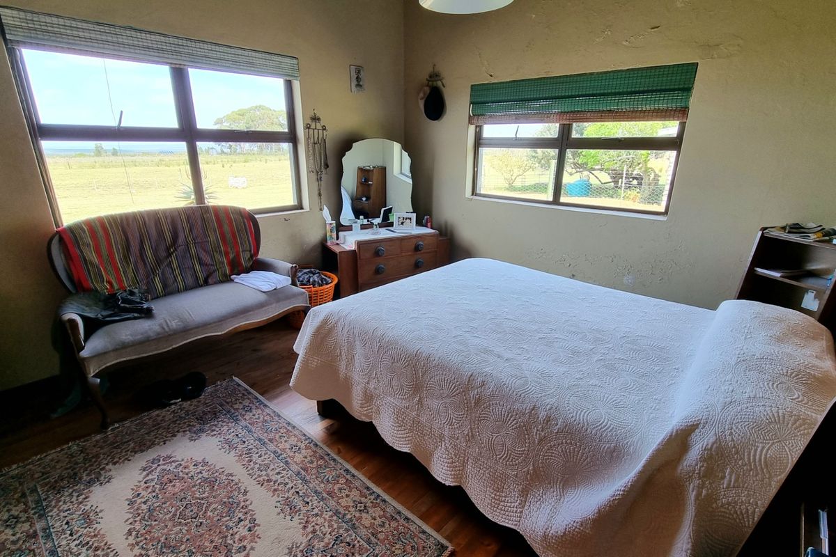 A rustic bedroom featuring timber flooring, large windows with rural views, and neutral wall finishes, offering a comfortable and well-lit living space.
