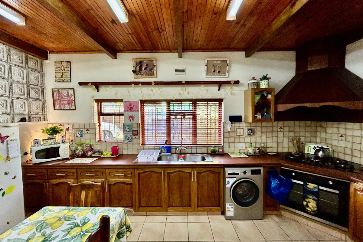 A rustic farm-style kitchen featuring timber cabinetry, a tiled backsplash, integrated oven and hob, and a timber-paneled ceiling with exposed beams.