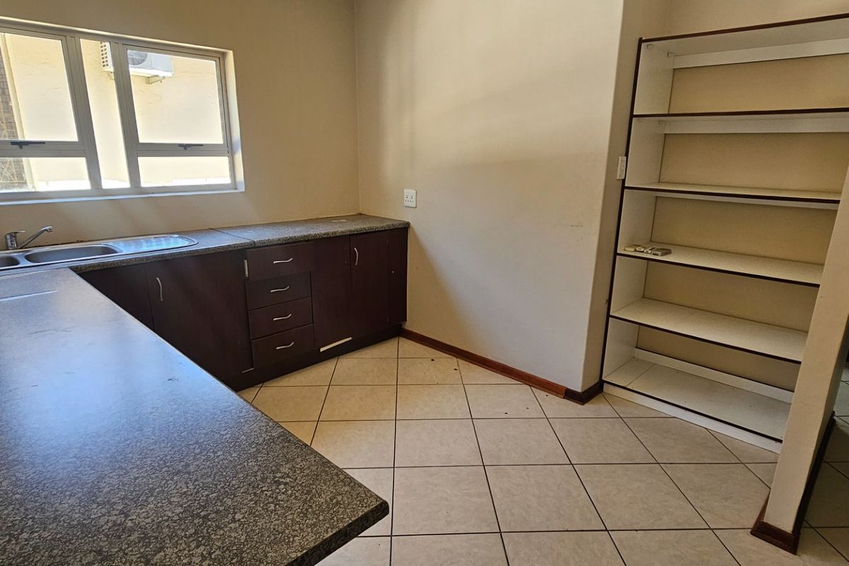 A functional kitchen area featuring dark cabinetry, stone-look laminate countertops, a stainless steel double sink, and built-in open shelving.