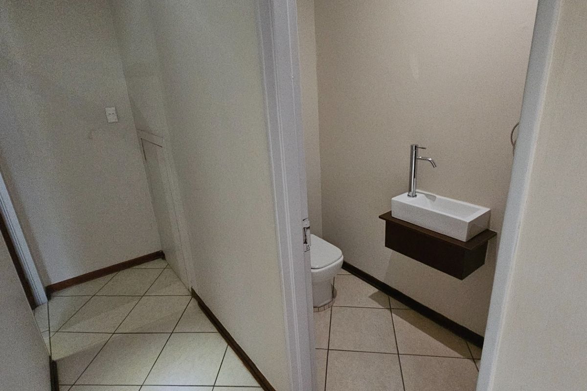 A compact guest bathroom featuring a wall-mounted basin and a toilet, finished with neutral wall paint and tiled flooring.