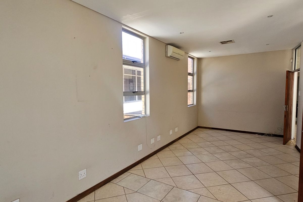 A spacious, empty room featuring tiled flooring, recessed ceiling lighting, and a wall-mounted air conditioning unit.