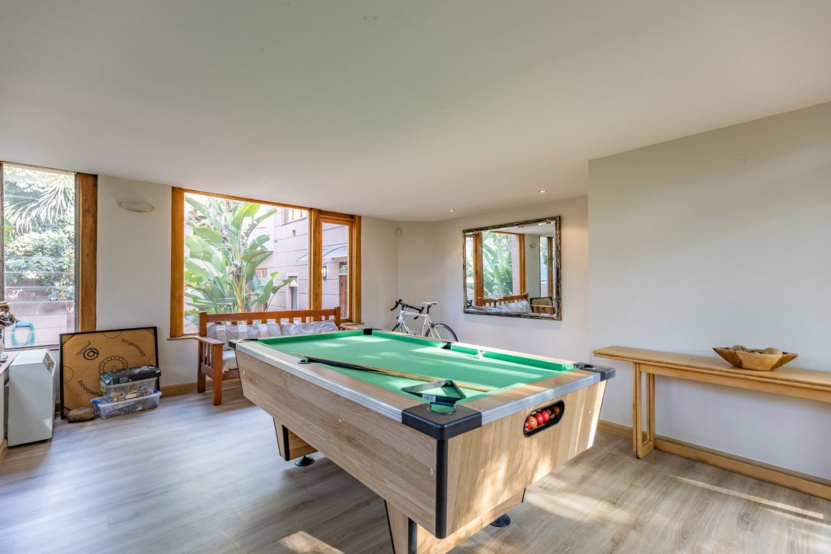 Spacious living area featuring large windows with garden views, wood-look flooring, and recessed lighting, currently utilized as a recreational space.