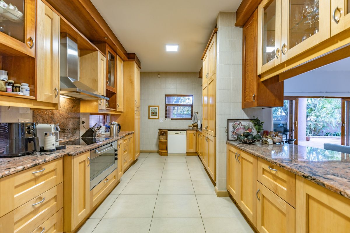 A functional galley-style kitchen featuring light wood cabinetry, granite countertops, integrated oven, stainless steel extractor fan, and tiled flooring.