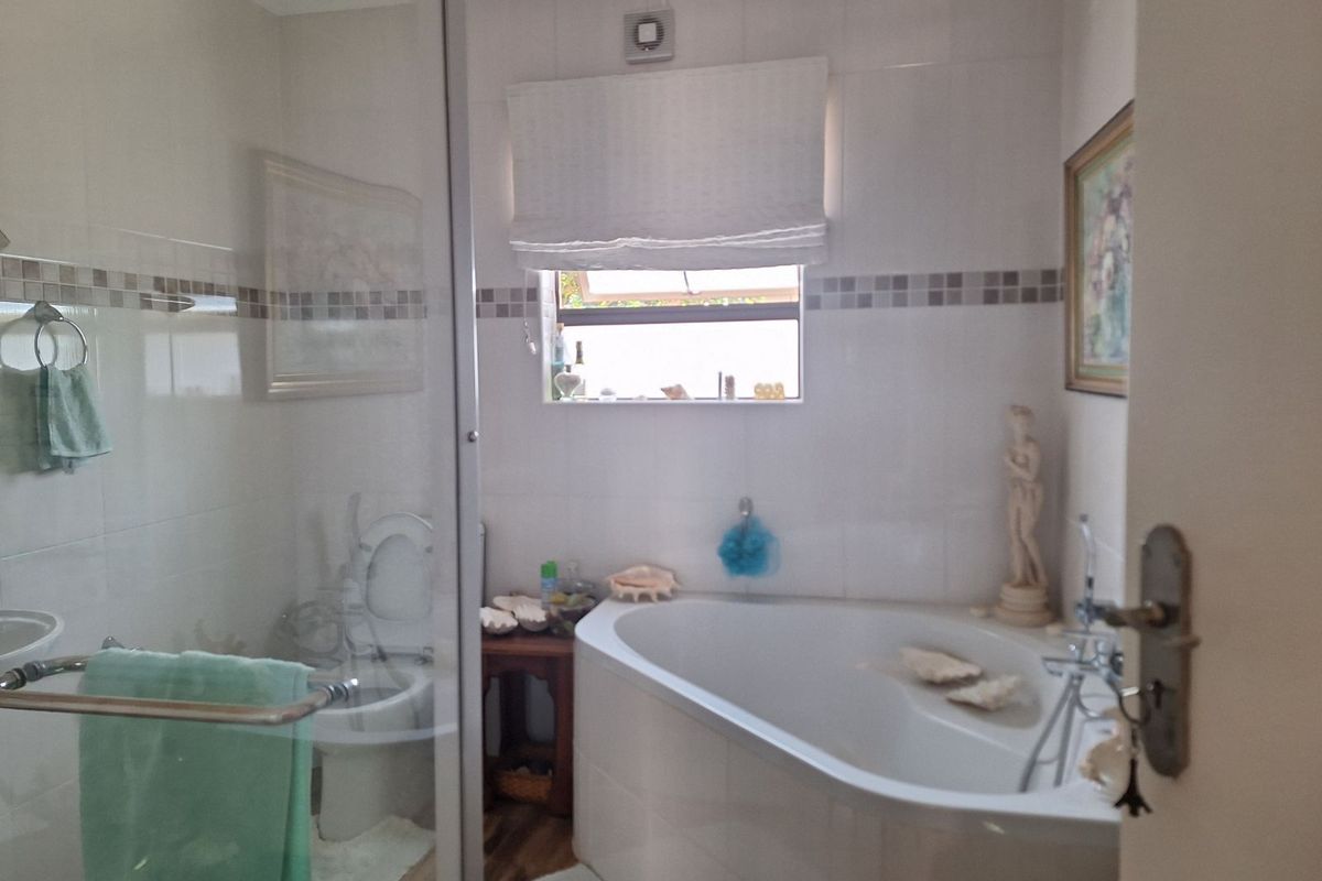 A functional bathroom featuring a corner bathtub, a glass-enclosed shower, and tiled walls with a decorative border.