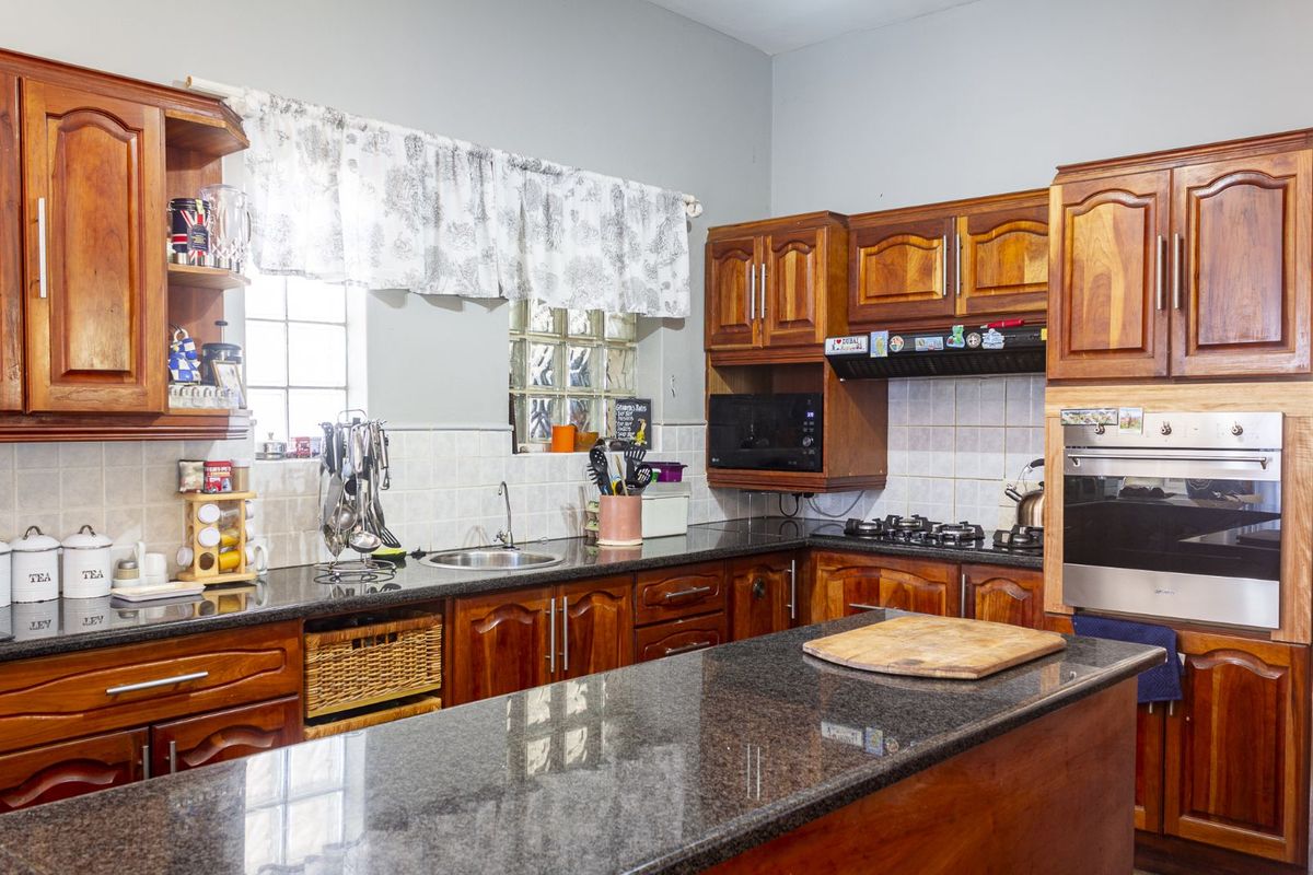 A functional kitchen featuring dark granite countertops, wooden cabinetry, a built-in oven, and a gas hob with an extractor fan.
