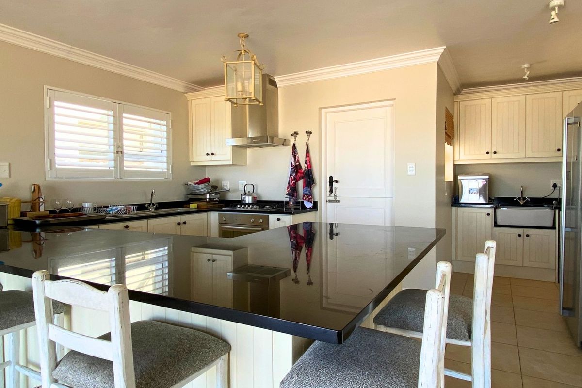 A well-appointed kitchen featuring a large central island with a dark stone countertop, cream cabinetry, stainless steel extractor fan, and integrated appliances.
