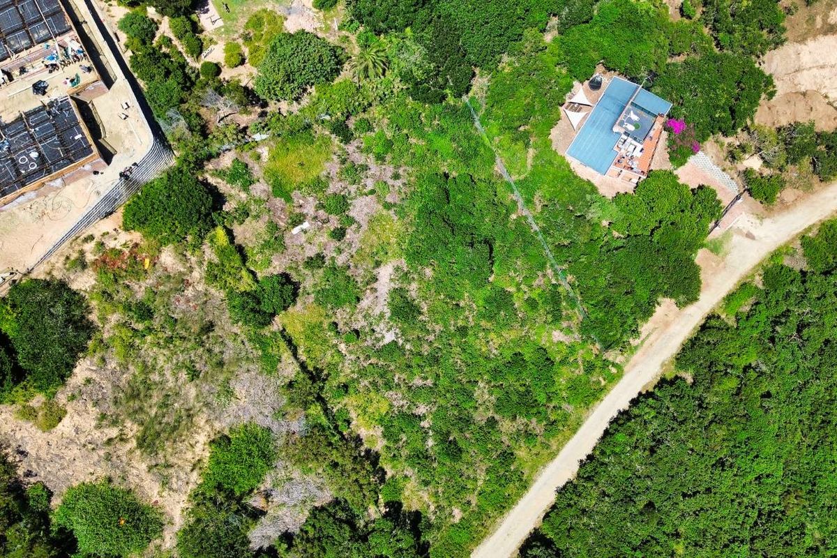 Aerial view of a vacant residential plot featuring natural vegetation, adjacent to existing residential development and a gravel access road.