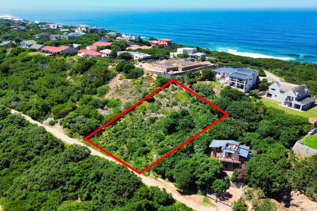 Aerial view of a vacant residential plot highlighted in red, situated in a coastal estate with surrounding indigenous vegetation and ocean views.