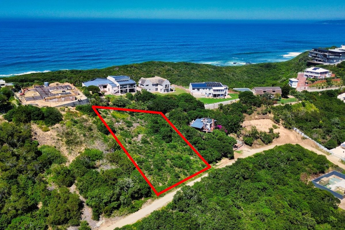 An aerial view of a vacant residential plot highlighted in red, situated in a coastal estate with ocean views and surrounding natural vegetation.