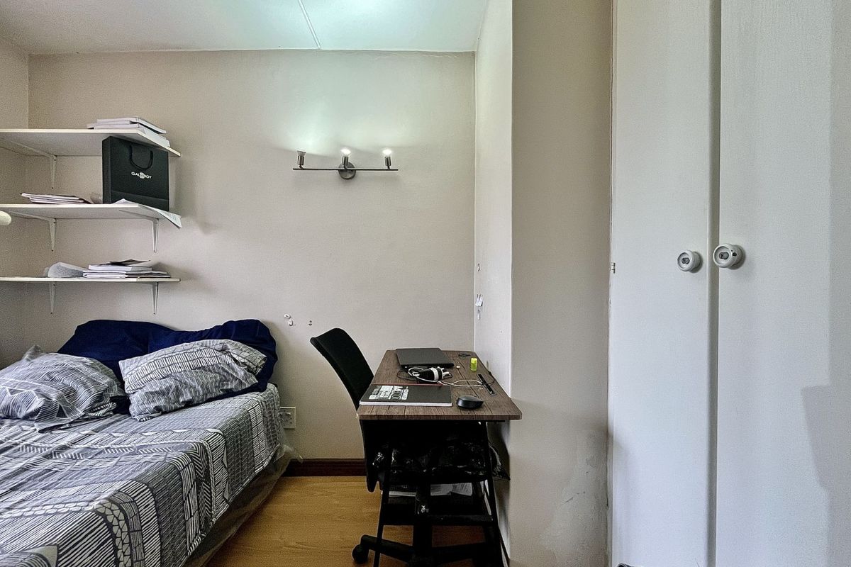 A functional bedroom featuring built-in storage cupboards, wall-mounted shelving, and laminate flooring, providing a practical living space.