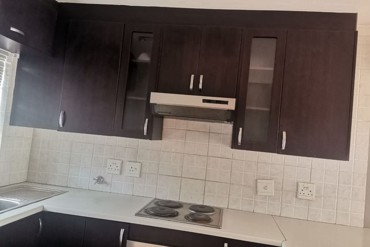 A functional kitchen featuring dark wood cabinetry, a built-in electric hob, extractor fan, and white tiled splashback with ample counter space.
