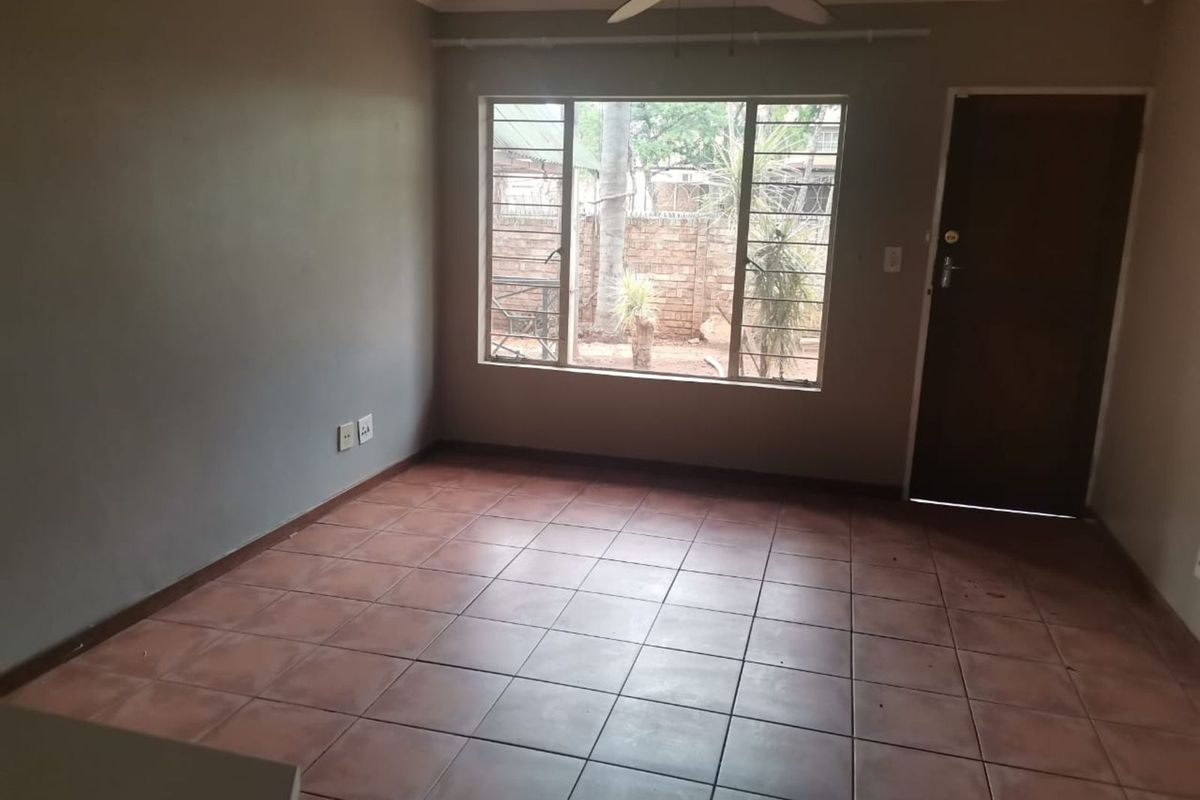 An empty living room featuring tiled flooring, a ceiling fan, and large windows providing natural light and a view of the exterior.