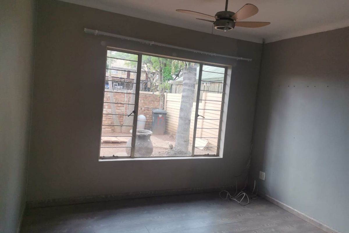 A vacant bedroom featuring laminate flooring, a ceiling fan, and a large window with security bars overlooking the rear garden area.