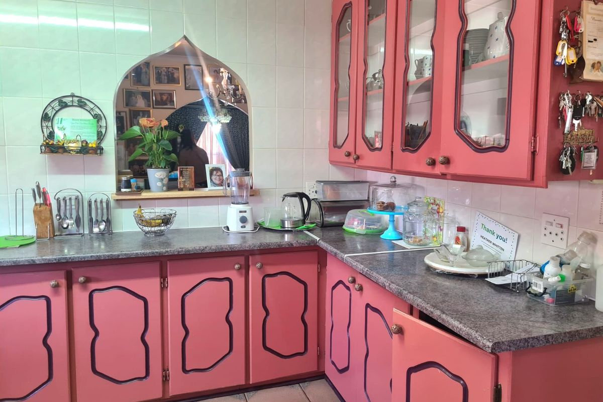 A dated kitchen featuring pink cabinetry with decorative trim, laminate countertops, and a tiled backsplash with a decorative arched wall opening.