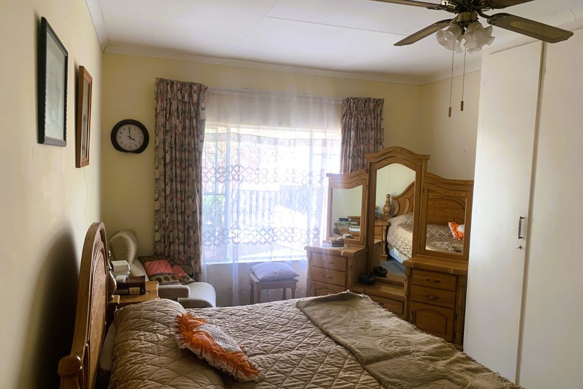 A bedroom featuring built-in cupboards, a ceiling fan, and large windows allowing natural light.