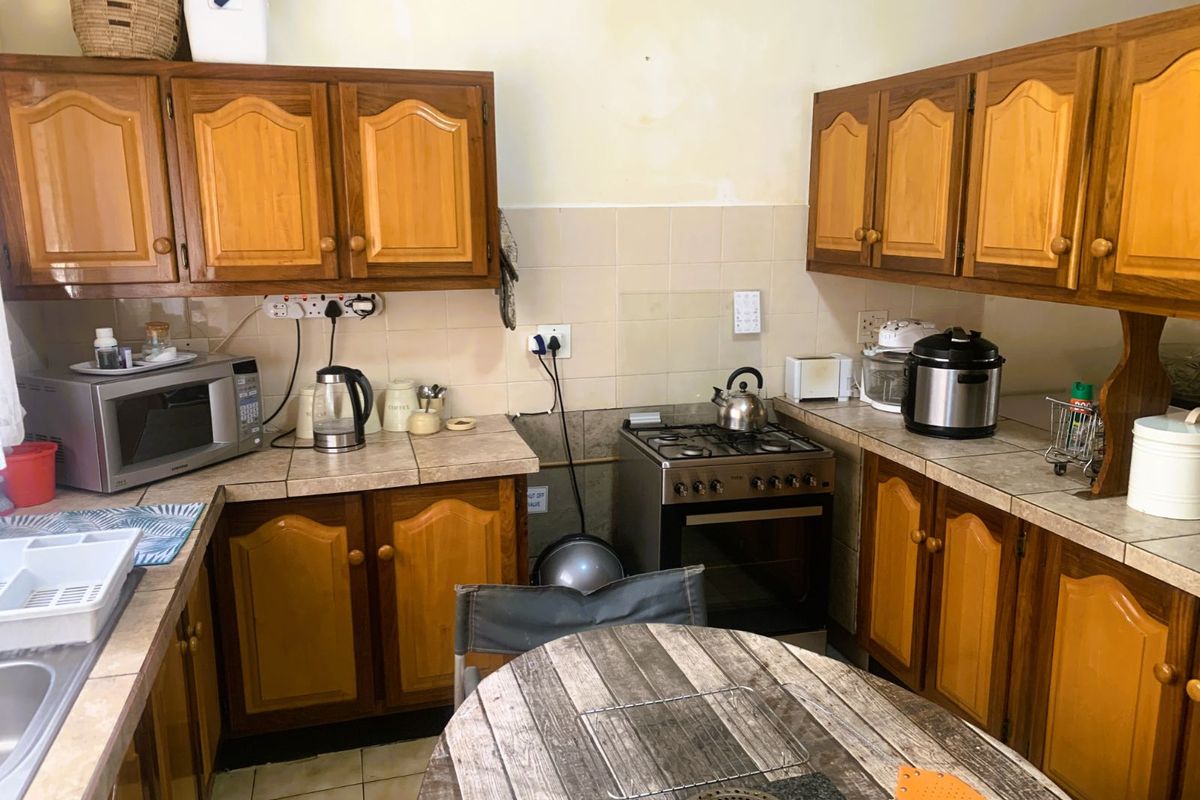 A functional kitchen featuring traditional wooden cabinetry, tiled countertops, and a built-in gas stove with oven, offering a classic layout with potential for modernization.