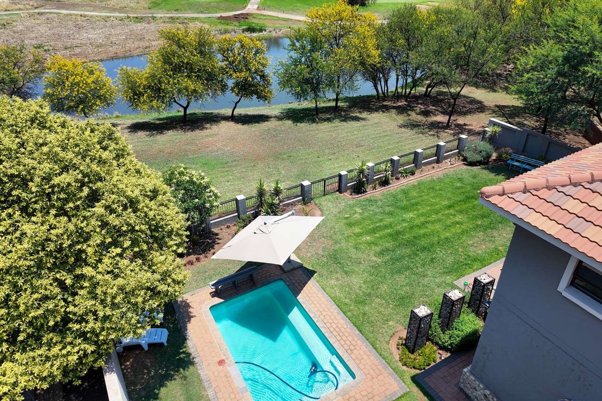Aerial view of a private backyard featuring a swimming pool, manicured lawn, perimeter fencing, and scenic views of a nearby pond and golf course.