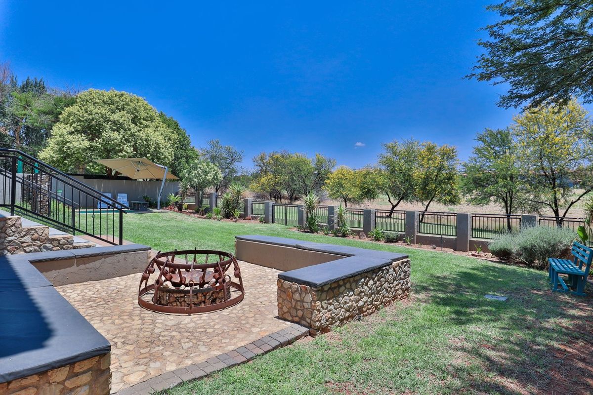 A landscaped rear garden featuring a stone-paved fire pit area with built-in stone seating, overlooking a spacious lawn and perimeter fencing.