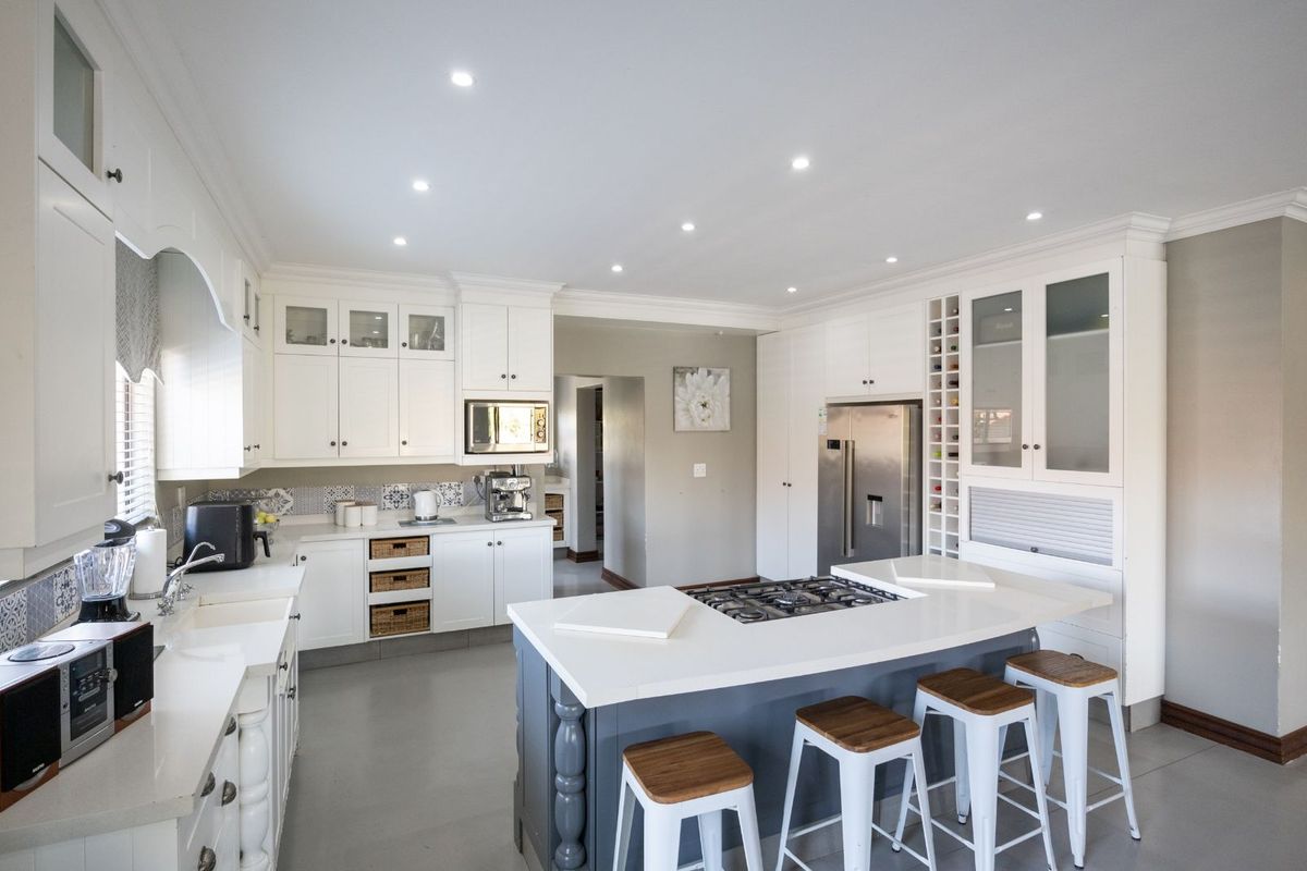 Modern kitchen featuring white cabinetry, stone countertops, a central island with a built-in gas hob, and integrated storage solutions.