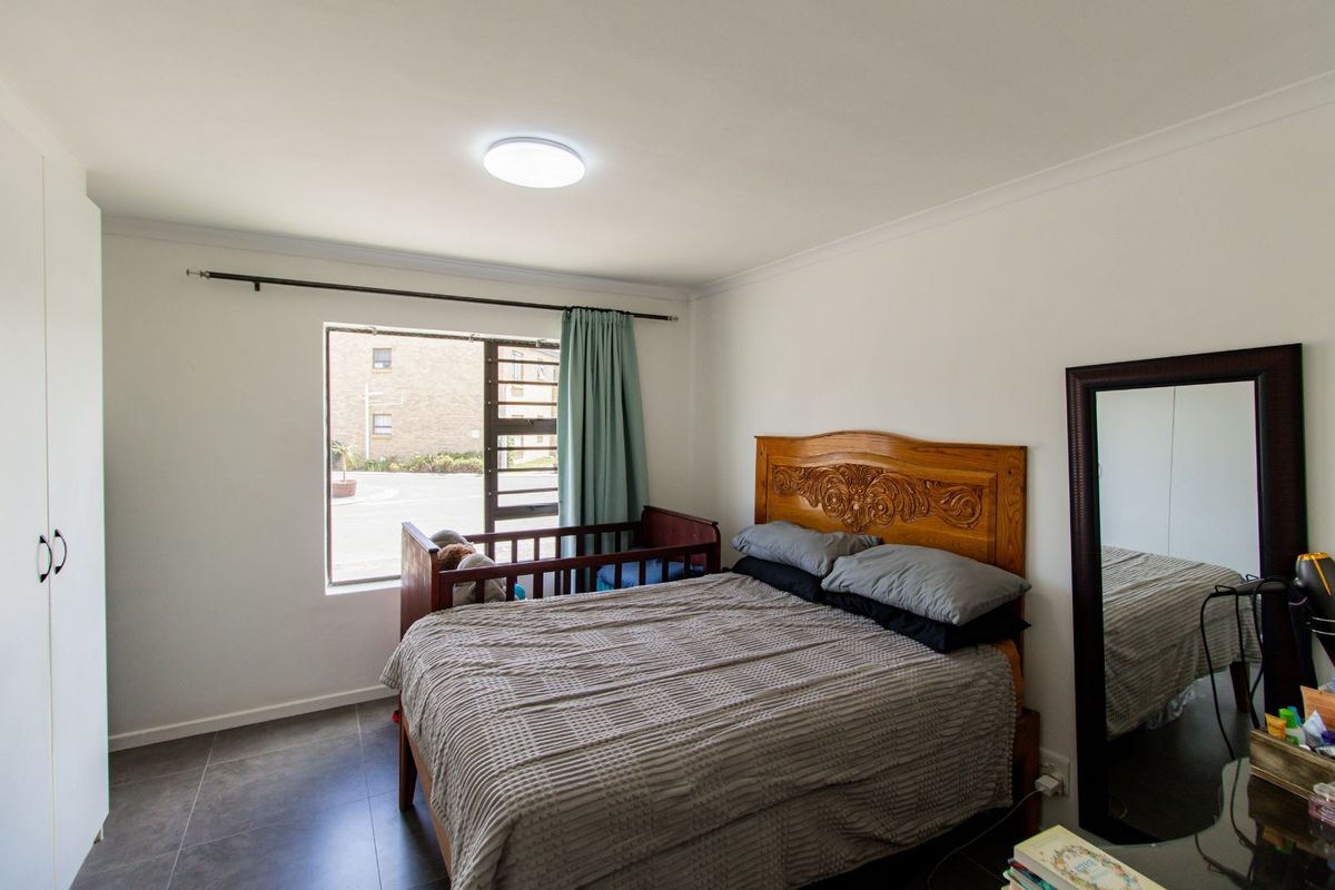 A well-lit bedroom featuring tiled flooring, built-in cupboards, and a large window providing natural light and exterior views.