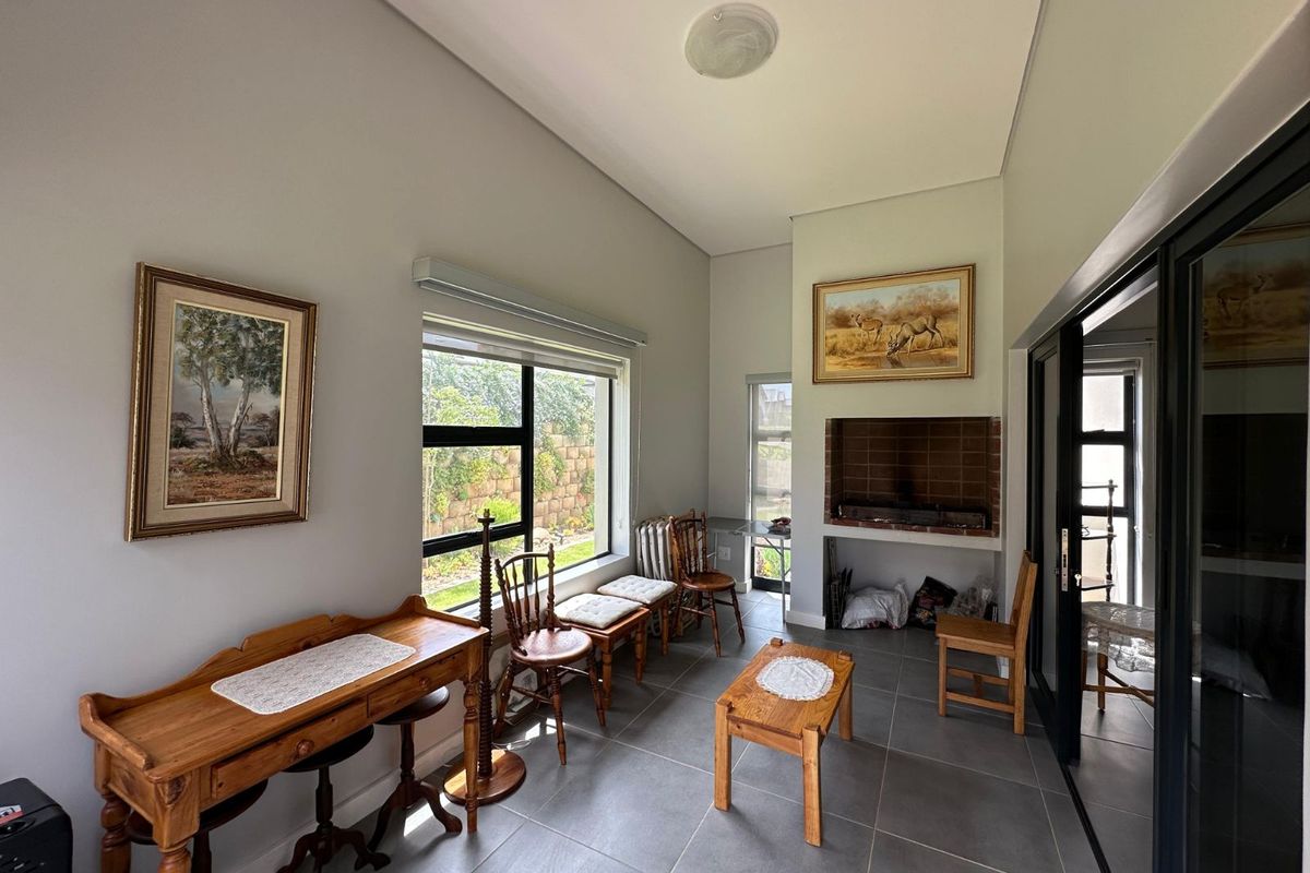 A living area featuring tiled flooring, a built-in brick fireplace, and large windows providing natural light and garden views.