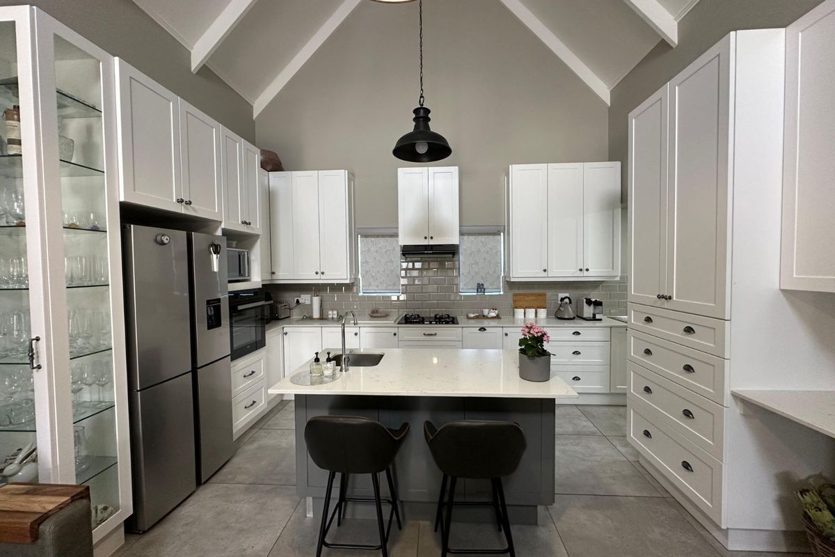 Modern kitchen featuring a vaulted ceiling, white cabinetry, central island with sink, stone countertops, and tiled flooring.