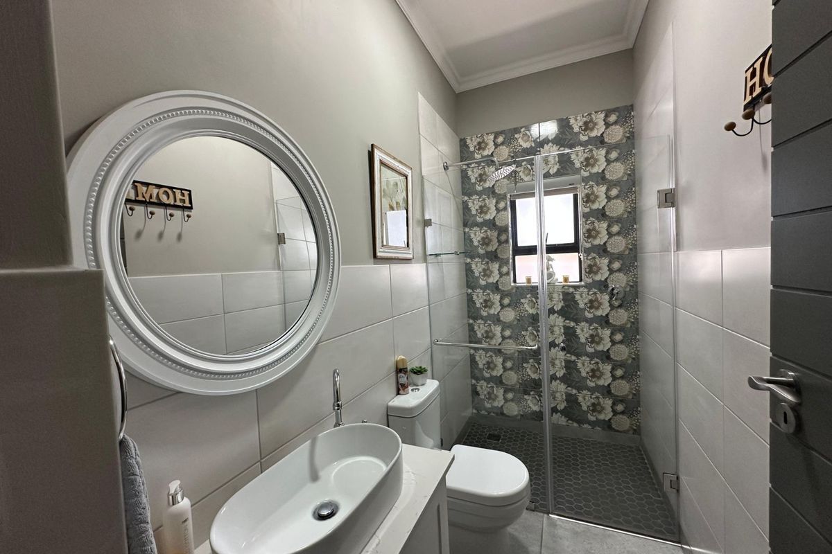 Modern bathroom featuring a glass-enclosed walk-in shower with decorative floral tiling, a vessel sink vanity, and a circular wall mirror.