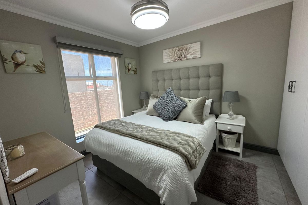 A well-maintained bedroom featuring tiled flooring, built-in cupboards, a ceiling fan with integrated lighting, and a large window providing natural light.