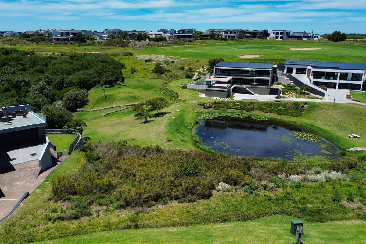 Aerial view of a modern residential property featuring landscaped grounds, a natural pond, and proximity to a golf course.